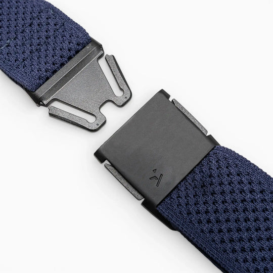 Close-up of the Arcade Belts Momentum stretch webbing strap in navy blue, featuring a black plastic clasp thats partly unfastened, shown on a light gray background.