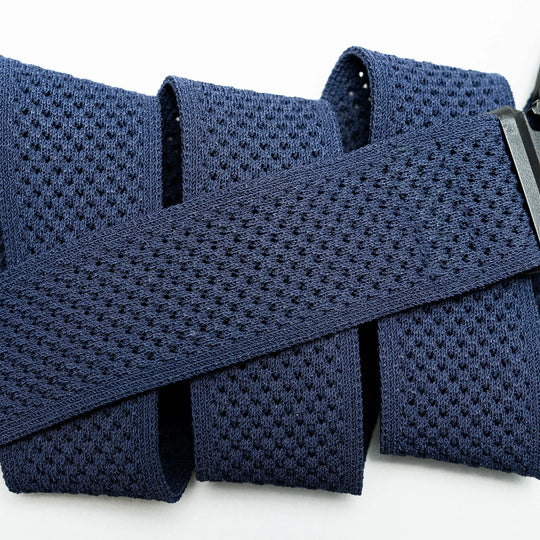 A close-up of the Momentum belt by Arcade Belts shows its navy blue perforated elastic strap, malleable webbing, and rectangular black buckle, with the comfortable strap folded in loops against a white background.