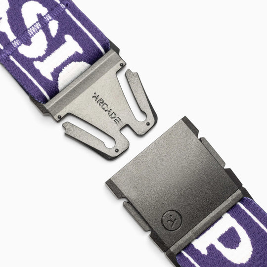Close-up of a black metal Arcade Belts buckle with the Mothership Classic name, paired with a purple and white patterned strap, shown partially unclasped against a white background—an accessory inspired by the adventurous spirit of events like the Mothership Classic in support of the High Fives Foundation.