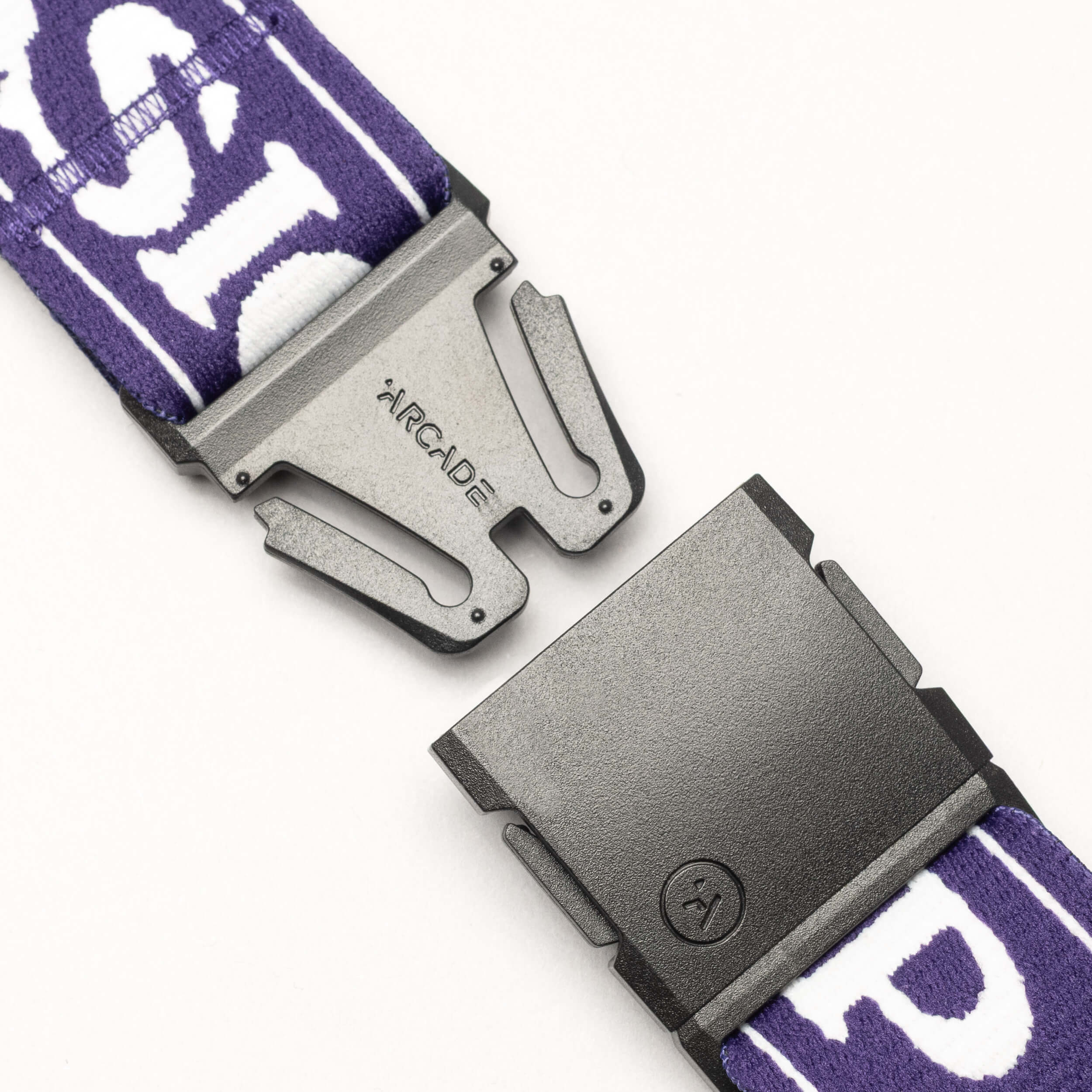 A close-up of the Arcade Belts Mothership Classic, a black plastic buckle engraved with ARCADE on a purple and white patterned belt, designed to honor the High Fives Foundation, shown partially unclasped on a white background.