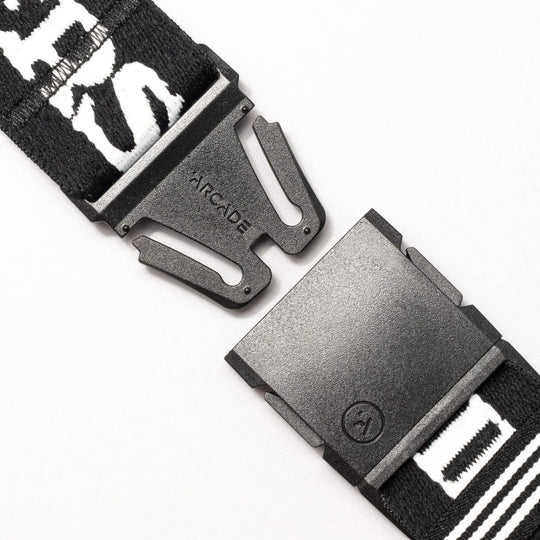 Close-up of the Arcade Belts Mothership Classic, featuring stretch webbing and a low profile. The black plastic buckle is partially unclipped, showing ARCADE on the metal piece. The strap displays white text and patterns.