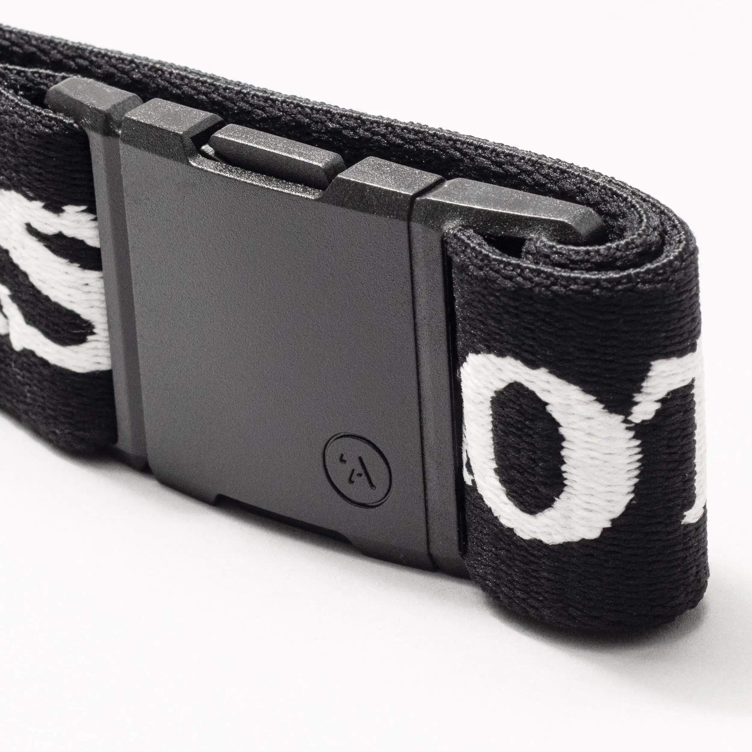 Close-up of Arcade Belts Mothership Classic: black stretch webbing strap with white embroidered letters and a rectangular plastic buckle, shown on a white background.