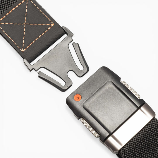 Close-up of the Motion belt by Arcade Belts, featuring a black textured fabric strap with orange stitching detail and an open quick-release metal buckle, offering a comfortable fit and modern style on a white background.