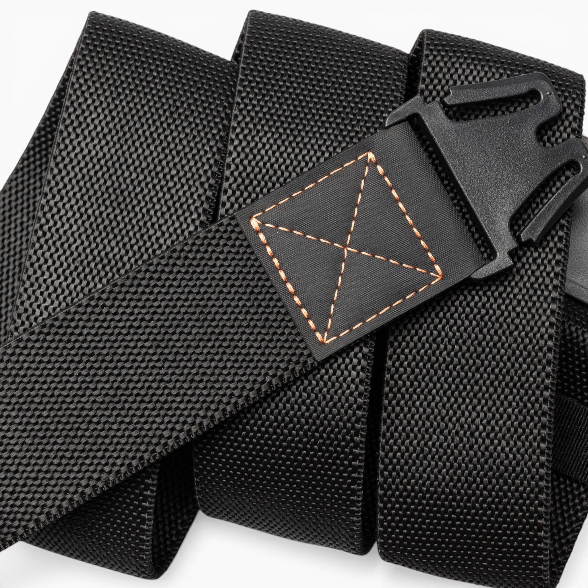 A close-up of the Arcade Belts Motion, a black nylon tactical belt featuring a plastic buckle and distinct orange stitching at the end. Coiled in a spiral shape, this belt is designed for a comfortable fit, seamlessly blending modern style with practicality.