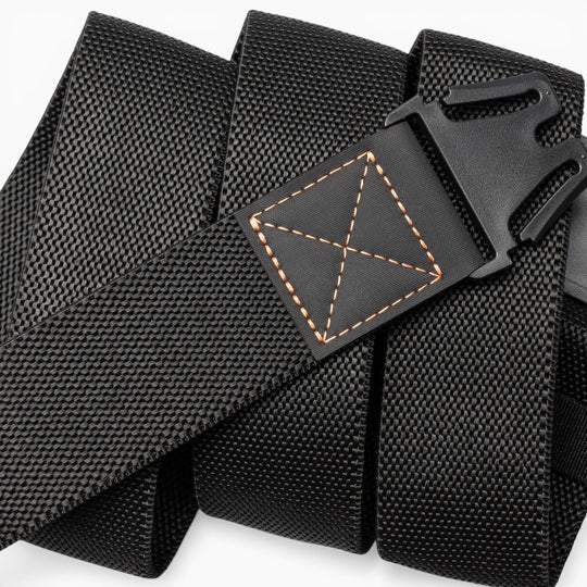 A close-up of the Arcade Belts Motion, a black nylon tactical belt featuring a plastic buckle and distinct orange stitching at the end. Coiled in a spiral shape, this belt is designed for a comfortable fit, seamlessly blending modern style with practicality.