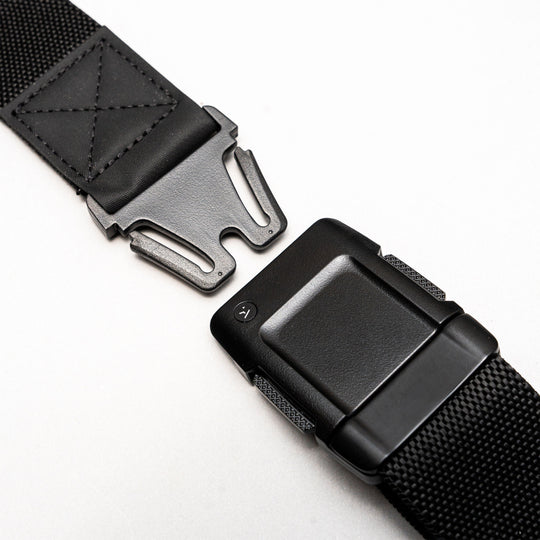 Close-up of the Arcade Belts Motion: a black low profile belt with a metal quick-release buckle, shown partially unfastened on a light background. Made from sturdy, textured stretch webbing for lasting durability and flexible comfort.