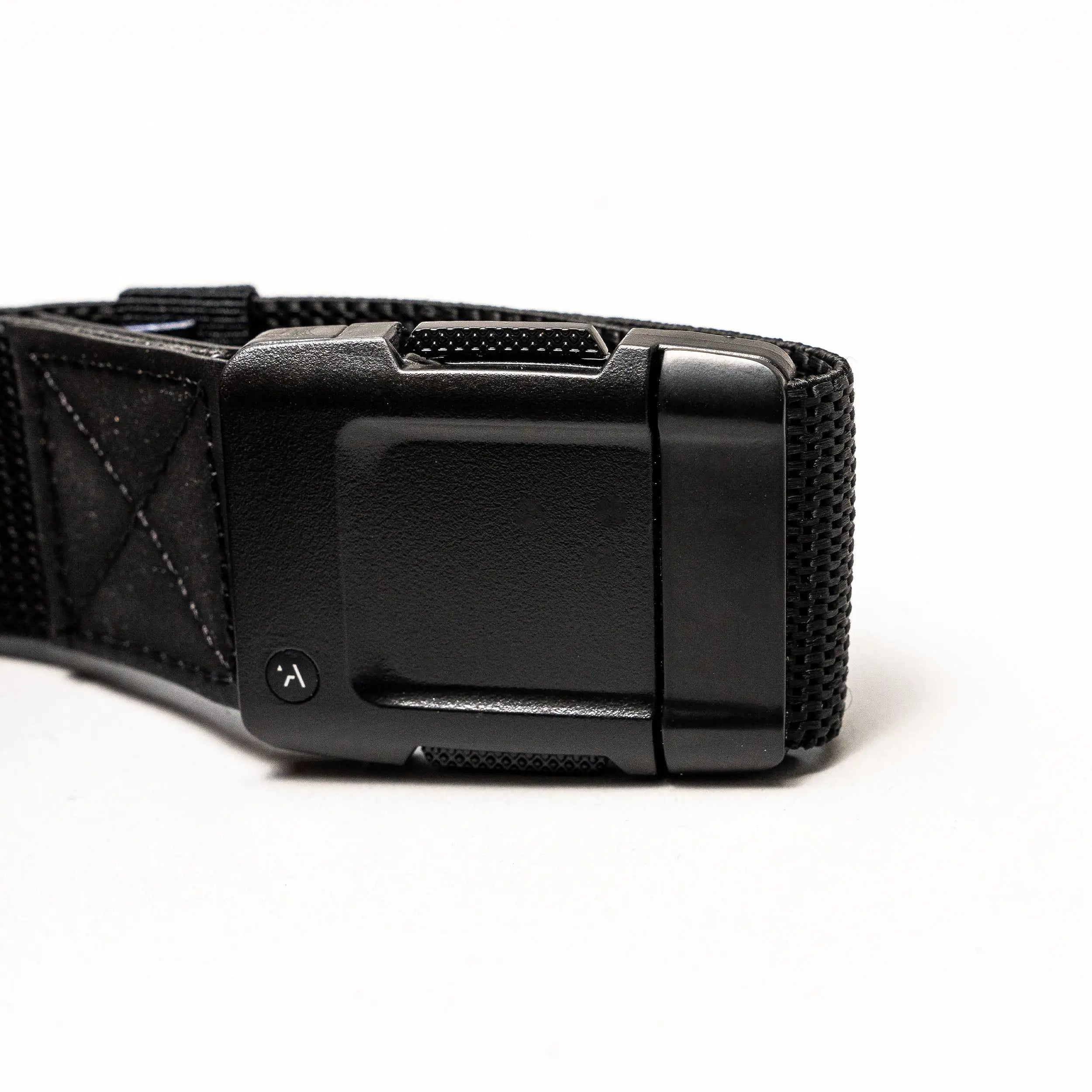 Close-up of the Arcade Belts Motion: a black fabric strap with a rectangular, textured plastic buckle on a white background. The buckle has a small round button with a curved arrow for secure fastening and easy adjustment—perfect for travel.