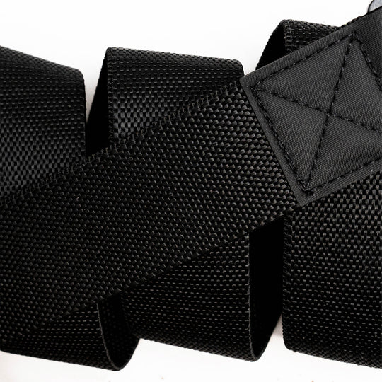 Close-up of the Arcade Belts Motion, a black textured woven strap with reinforced stitching at one end, coiled in a zigzag pattern against a white background.