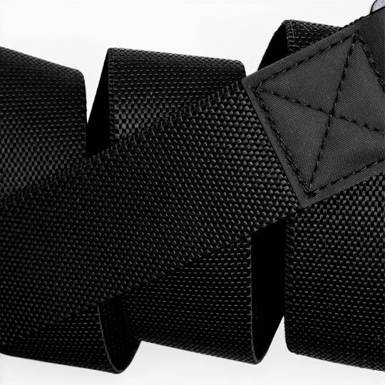 Close-up of the Arcade Belts Motion, a black textured woven strap with reinforced stitching at one end, coiled in a zigzag pattern against a white background.