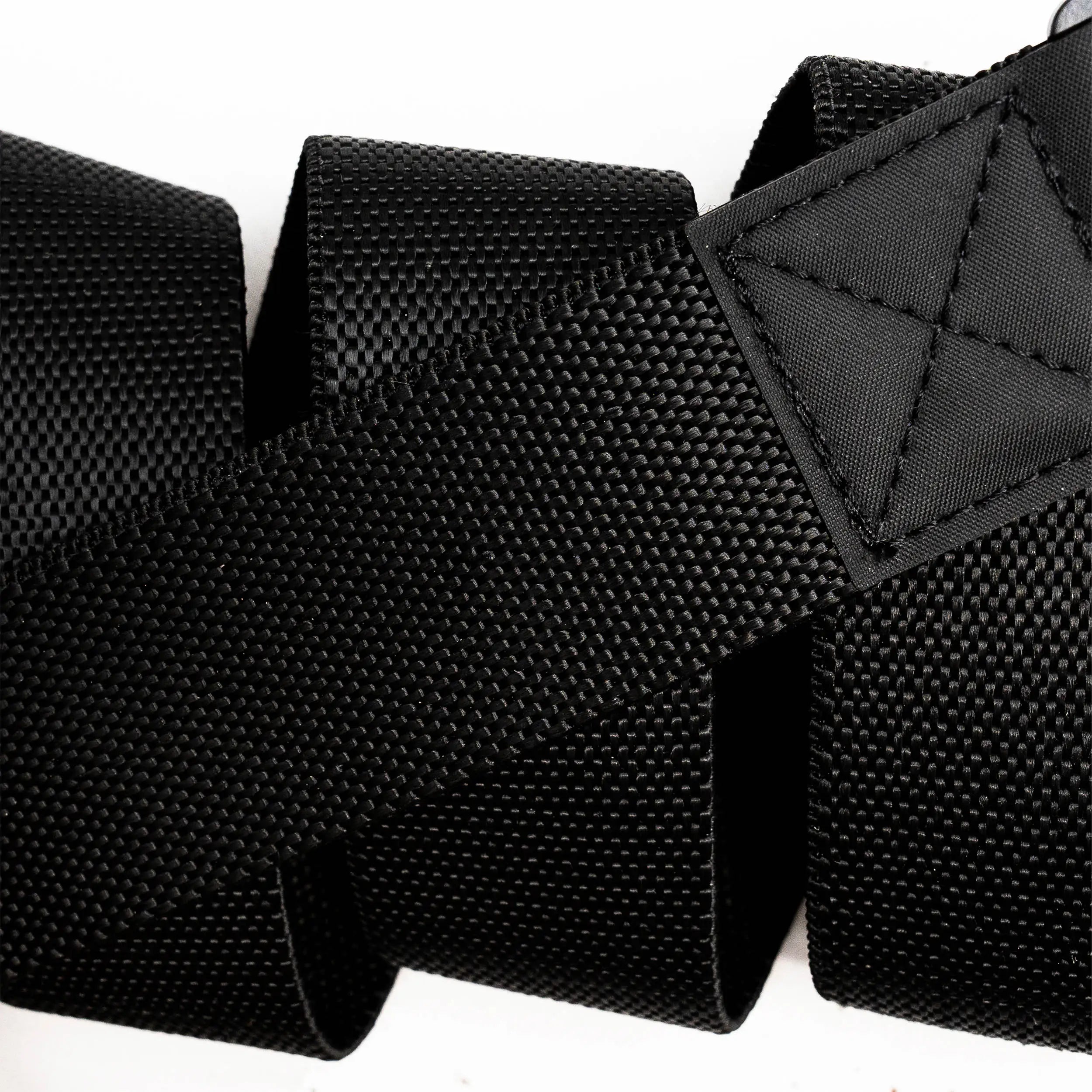 Close-up of the Arcade Belts Motion, a black textured woven strap with reinforced stitching at one end, coiled in a zigzag pattern against a white background.