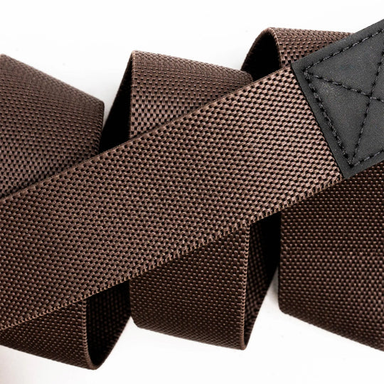 Close-up of the Arcade Belts Motion belt, featuring brown textured nylon stretch webbing and a black stitched patch, coiled loosely on a white background.