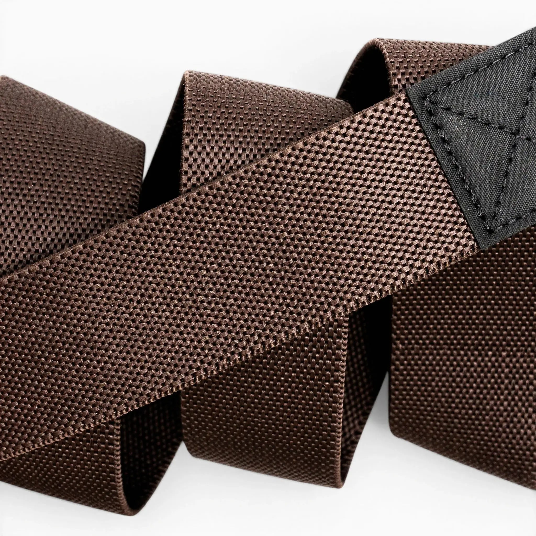 Close-up of the Arcade Belts Motion belt, featuring brown textured nylon stretch webbing and a black stitched patch, coiled loosely on a white background.