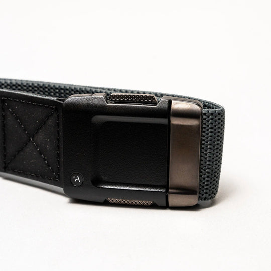 A close-up of the Arcade Belts Motion, a gray performance stretch belt with a black and metallic rectangular buckle, highlights its comfortable fit and modern style on a light background.