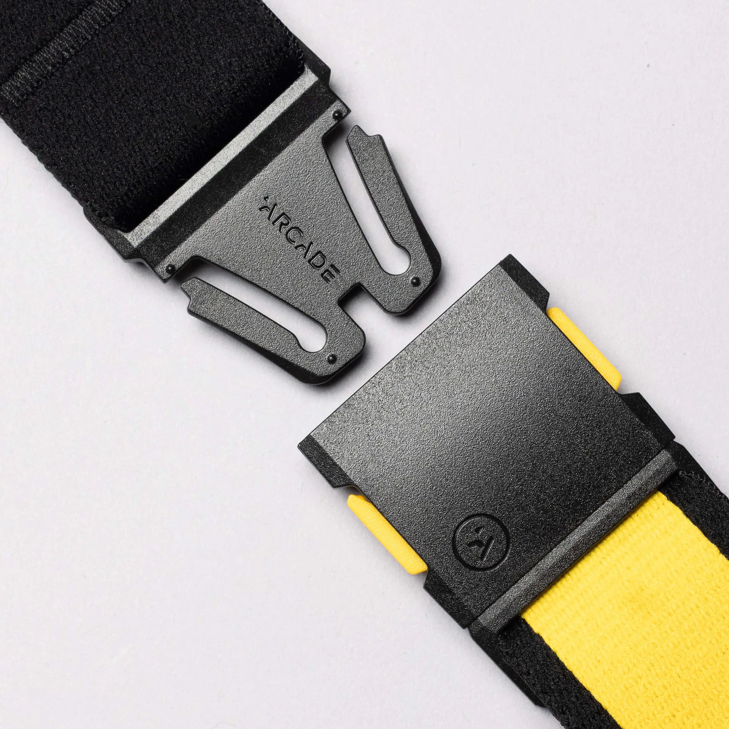 A close-up of the Arcade Belts National Geographic adjustable belt in black and yellow with a black metal buckle, featuring the embossed Arcade logo. The buckle is partially unclasped against a light gray background.