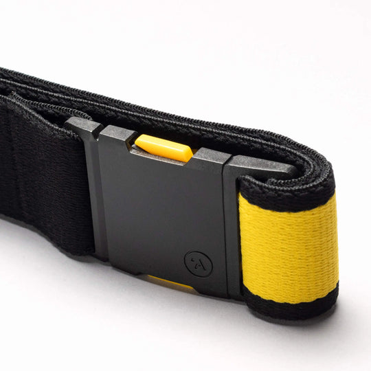 A close-up of the Arcade Belts National Geographic strap: black with a black plastic buckle, yellow accent, and yellow fabric-wrapped end with a black stripe. Features a distinctive yellow button release—ideal for adventures.