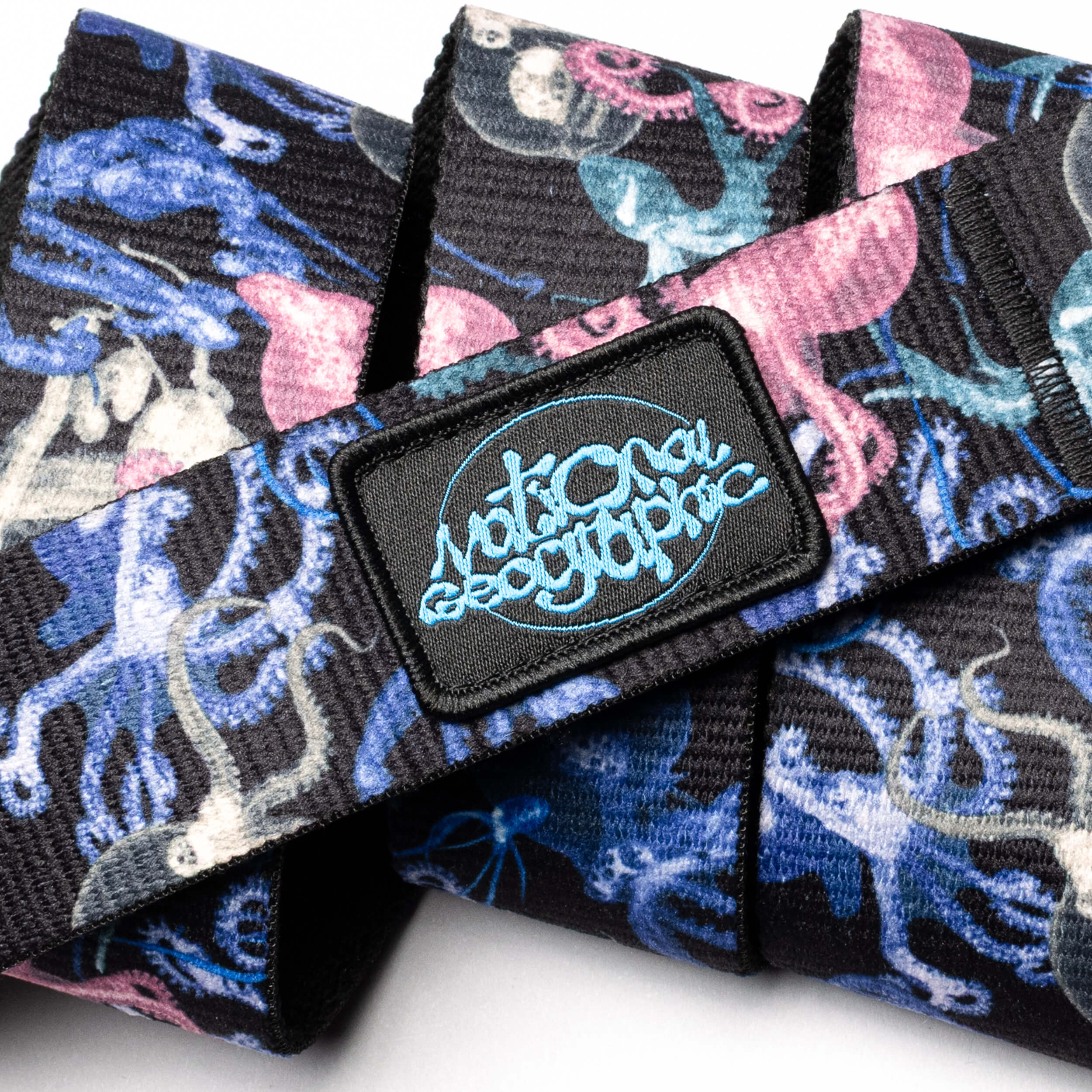 A close-up of the Arcade Belts "National Geographic" fabric belt with a vibrant pink, blue, and white octopus pattern and a black patch showcasing blue "National Geographic" branding.
