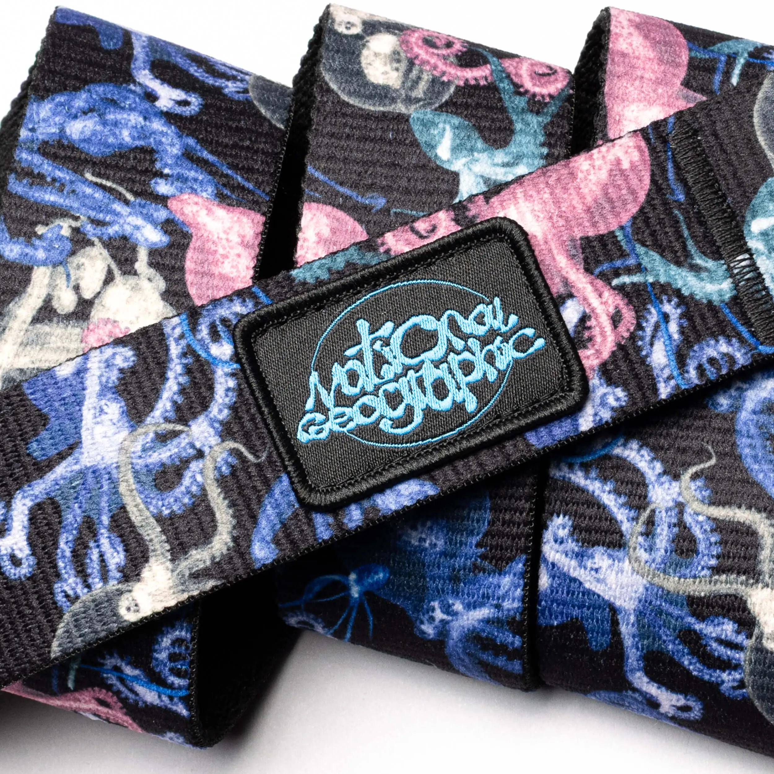 A close-up of the Arcade Belts "National Geographic" fabric belt with a vibrant pink, blue, and white octopus pattern and a black patch showcasing blue "National Geographic" branding.