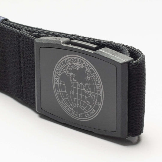 Close-up of the Arcade Belts National Geographic 1888 black low profile belt with a rectangular buckle engraved with the National Geographic Society globe logo and text, shown on a plain white background.