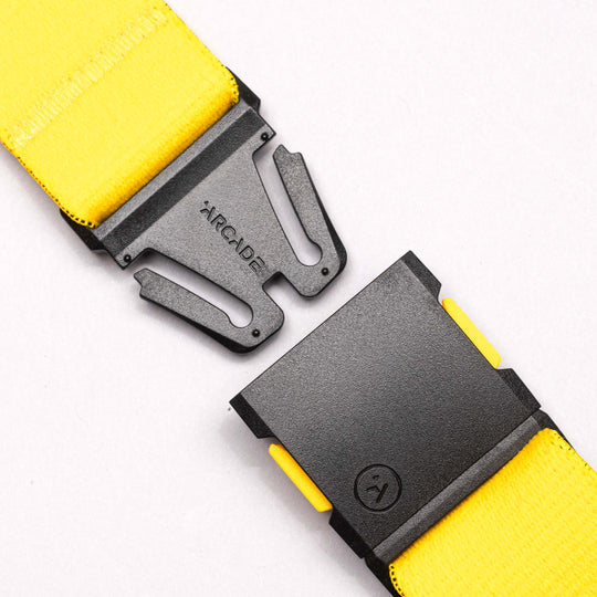 A close-up of a yellow National Geographic belt by Arcade Belts, featuring a black, partially unclasped low-profile buckle engraved with ARCADE, set against a plain white background.