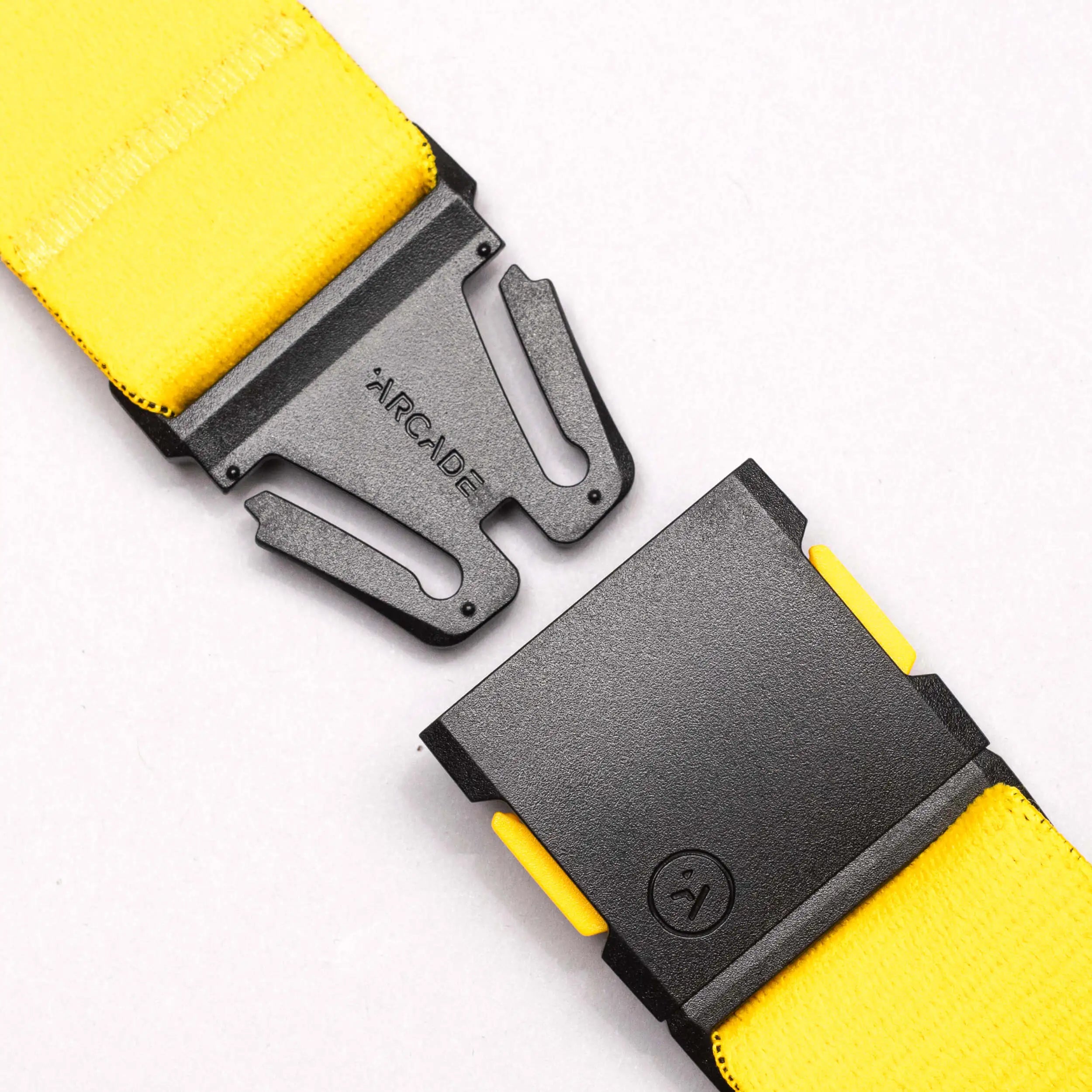 A close-up of a yellow National Geographic belt by Arcade Belts, featuring a black, partially unclasped low-profile buckle engraved with ARCADE, set against a plain white background.