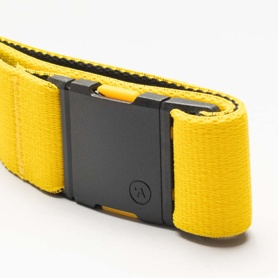 A close-up of an Arcade Belts National Geographic yellow Low Profile Belt with a black rectangular buckle, made from stretch webbing and shown on a plain white background.