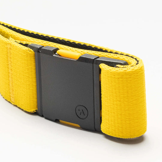A close-up of an Arcade Belts National Geographic yellow Low Profile Belt with a black rectangular buckle, made from stretch webbing and shown on a plain white background.