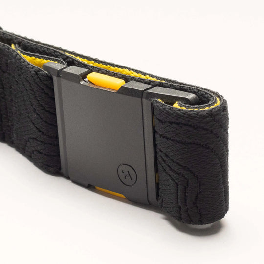 A close-up of the National Geographic by Arcade Belts: a black buckle with yellow accents on textured black webbing, set against a white background—ideal for travel belt fans.