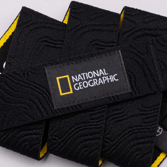 Close-up of a black stretch webbing strap from Arcade Belts for National Geographic, with embossed patterns and a stitched label featuring the iconic yellow rectangle and white logo.
