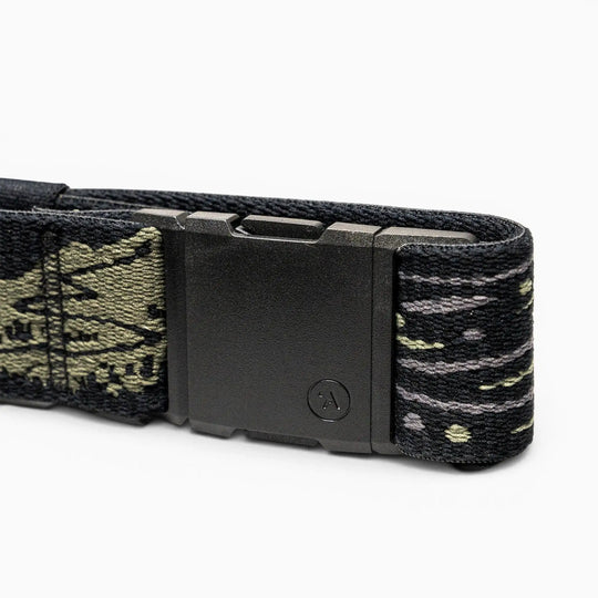 A close-up of the Arcade Belts Out of Range belt shows a black rectangular buckle and stretch webbing with a green and gray camo pattern. A small circular A logo decorates the buckle, ensuring both comfort and branded style.