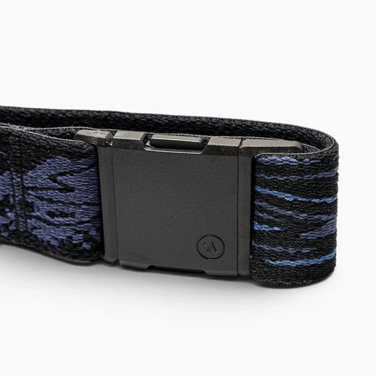 A close-up of the Arcade Belts Out of Range black plastic buckle on an elastic stretch belt with a dark blue and black patterned strap, shown against a white background.