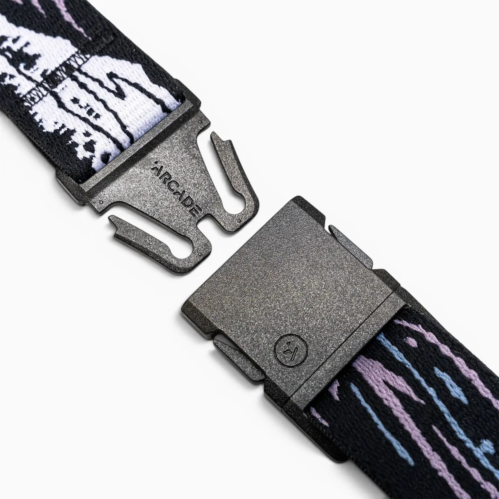 A close-up of the Arcade Belts Slim Kit shows its black plastic buckle on a stretch web strap with white, black, purple, and blue patterns, unclasped on a white background—perfect as a low-profile belt.