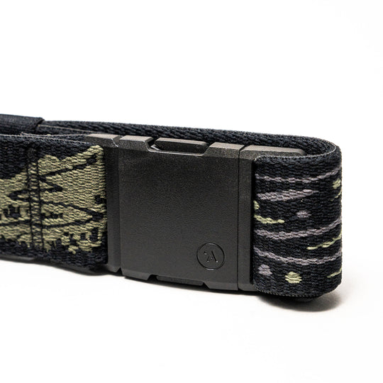 A close-up of the Arcade Belts Out of Range belt shows a black rectangular buckle and stretch webbing with a green and gray camo pattern. A small circular A logo decorates the buckle, ensuring both comfort and branded style.