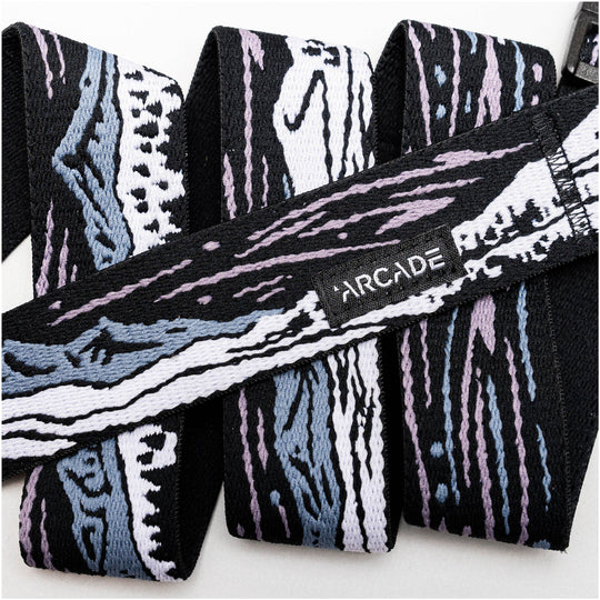 A close-up of the Arcade Belts Out of Range elastic stretch belt with an abstract black, white, blue, and lavender pattern, featuring a small black label stitched with white ARCADE text.