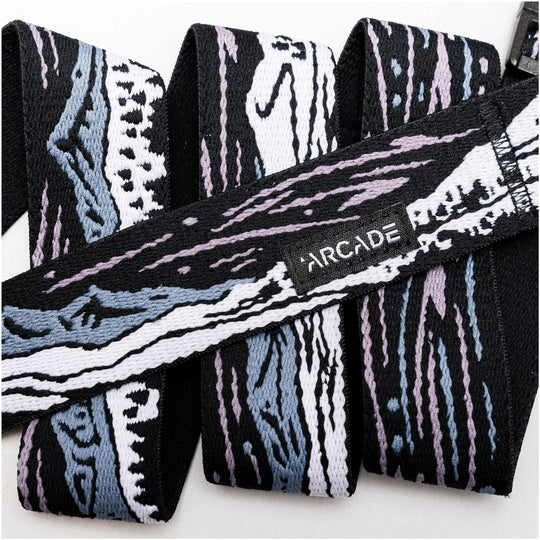 A close-up of the Arcade Belts Out of Range elastic stretch belt with an abstract black, white, blue, and lavender pattern, featuring a small black label stitched with white ARCADE text.