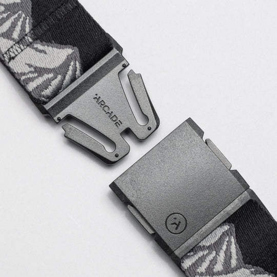 A close-up of the Arcade Belts POW x Joseph Toney, a black belt with gray and white patterns, features an open black buckle and ARCADE branding, showcasing its low-profile design.