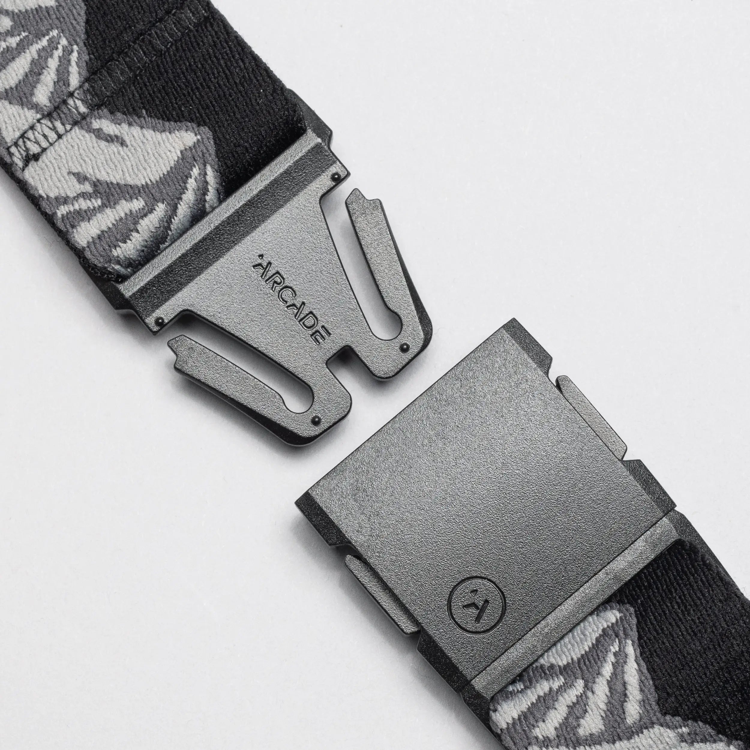 A close-up of the Arcade Belts POW x Joseph Toney, a black belt with gray and white patterns, features an open black buckle and ARCADE branding, showcasing its low-profile design.