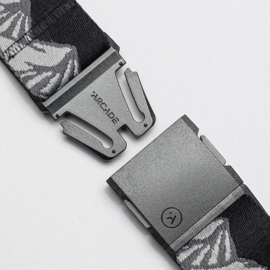 A close-up of the Arcade Belts POW x Joseph Toney, a black belt with gray and white patterns, features an open black buckle and ARCADE branding, showcasing its low-profile design.