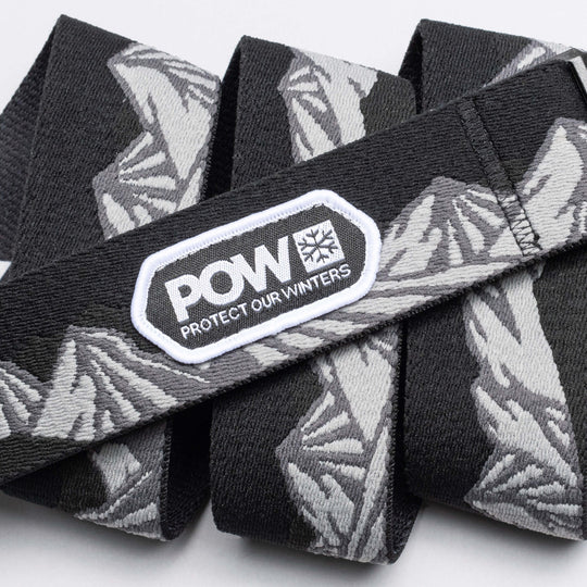 The Arcade Belts POW x Joseph Toney is a black and gray stretch webbing belt with mountain patterns, a low profile design, and a white POW PROTECT OUR WINTERS patch—showcasing classic Arcade Belts style.