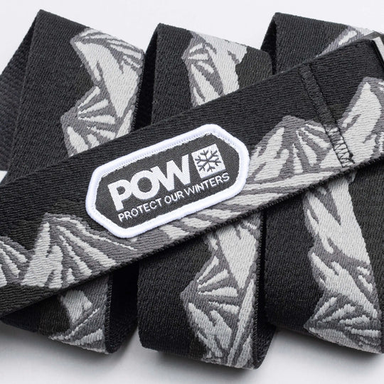 The Arcade Belts POW x Joseph Toney is a black and gray stretch webbing belt with mountain patterns, a low profile design, and a white POW PROTECT OUR WINTERS patch—showcasing classic Arcade Belts style.