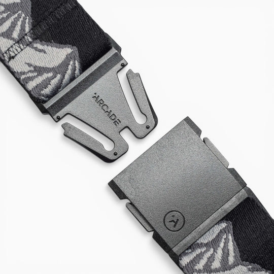 A close-up of the Arcade Belts POW x Joseph Toney, a black belt with gray and white patterns, features an open black buckle and ARCADE branding, showcasing its low-profile design.