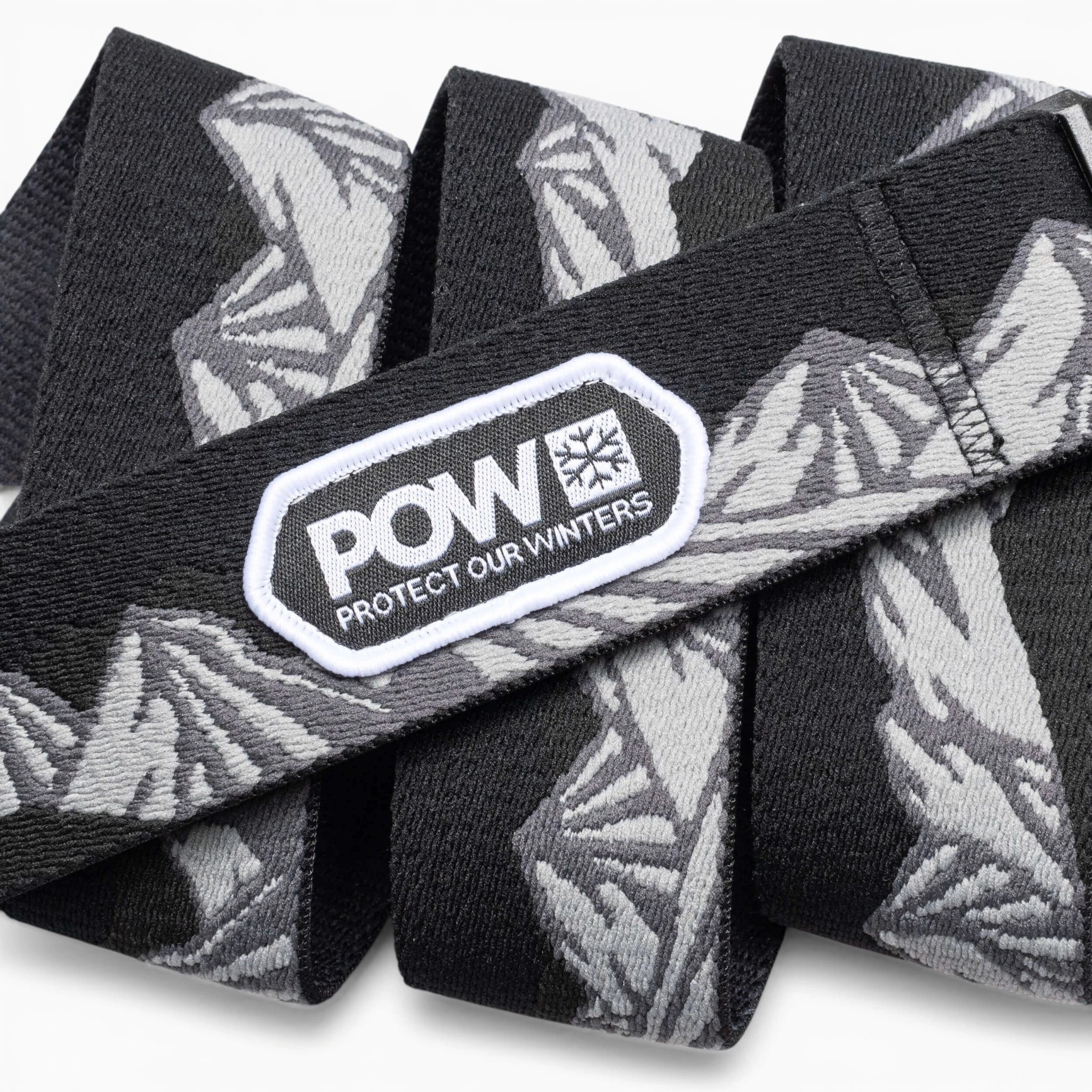 The Arcade Belts POW x Joseph Toney is a black and gray stretch webbing belt with mountain patterns, a low profile design, and a white POW PROTECT OUR WINTERS patch—showcasing classic Arcade Belts style.