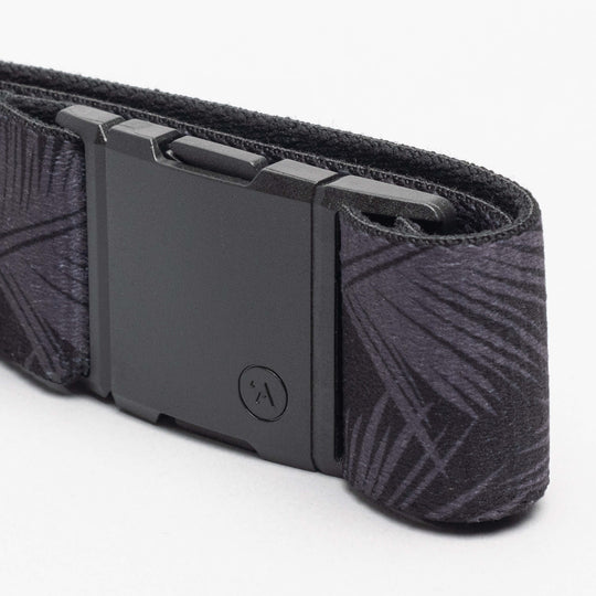 A close-up of the Arcade Belts Island Collection: a black fabric belt with a geometric Hawaiian-inspired pattern and a matte black rectangular buckle, coiled on a plain white background.