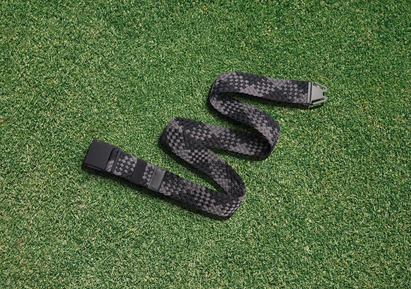 A black and gray checkered belt is laid out in a zigzag shape on green grass.