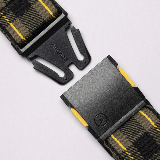 Close-up of a black metal buckle engraved with "ARCADE," attached to the new limited-edition Plaid strap from Arcade Belts in yellow, black, and gray—showcased against a light background.