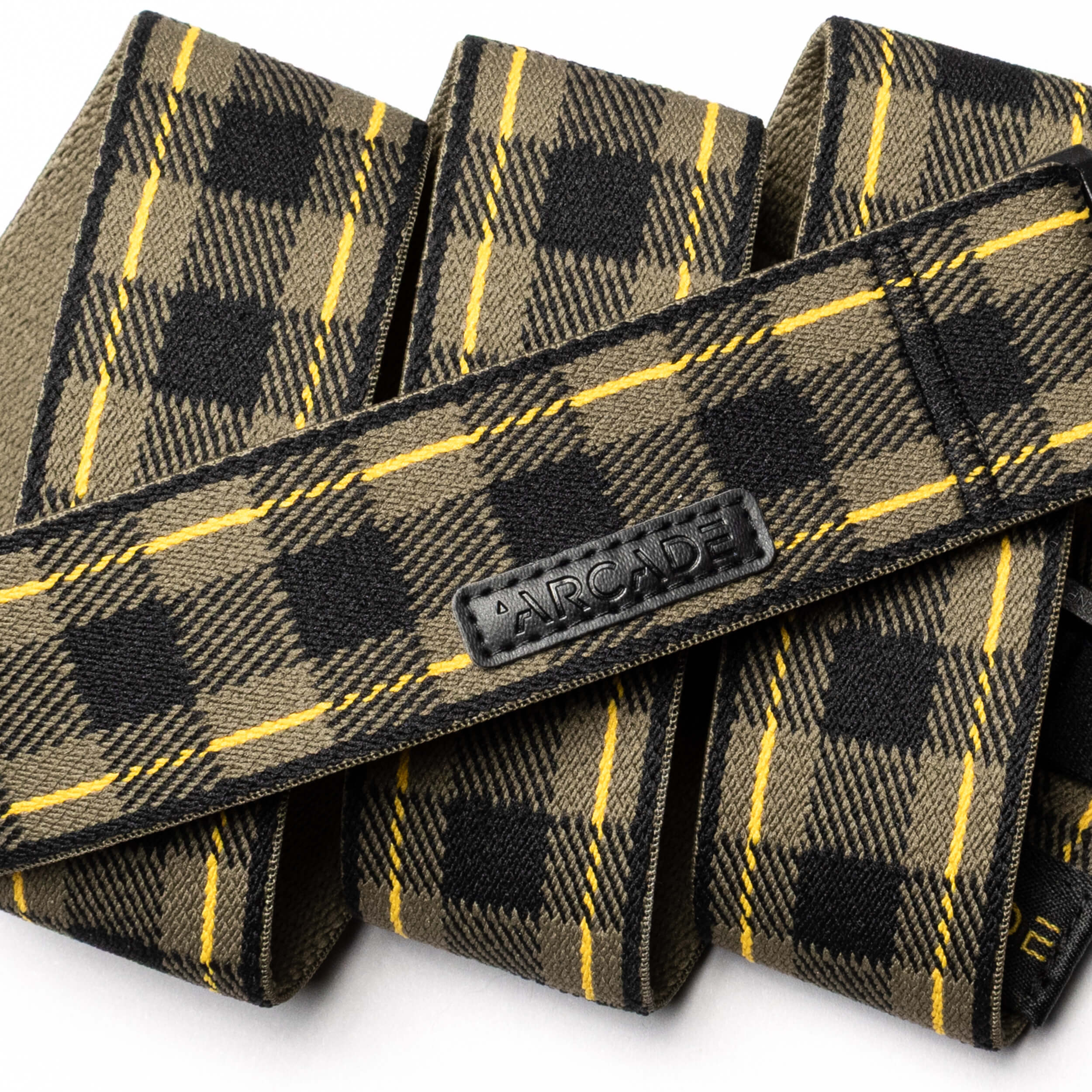 A close-up of the Plaid belt by Arcade Belts in olive green, black, and yellow with a black ARCADE logo patch. Displayed in overlapping folds on a white background, this limited-edition style features new colors.