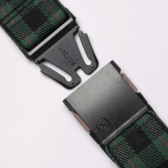 Close-up of the Plaid Elastic Stretch Belt by Arcade Belts, featuring a green and black plaid pattern and a black ARCADE-labeled metal buckle, shown partially unbuckled on a light background.