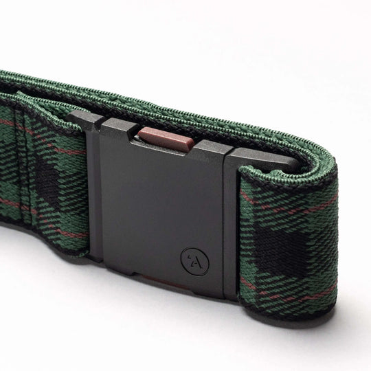 A close-up of the Plaid belt by Arcade Belts shows green and black stretch webbing with a red-accented checkered pattern, plus a rectangular black buckle with a small circular logo—ideal for travel belt fans.