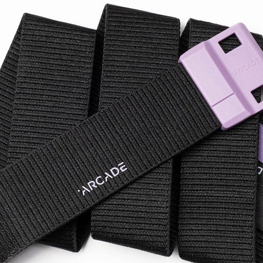 A close-up of the Arcade Belts Polar, a black belt with a purple rectangular plastic buckle featuring SwiftLock technology, displayed on a white background. It has a subtle ribbed texture and the white Arcade logo.