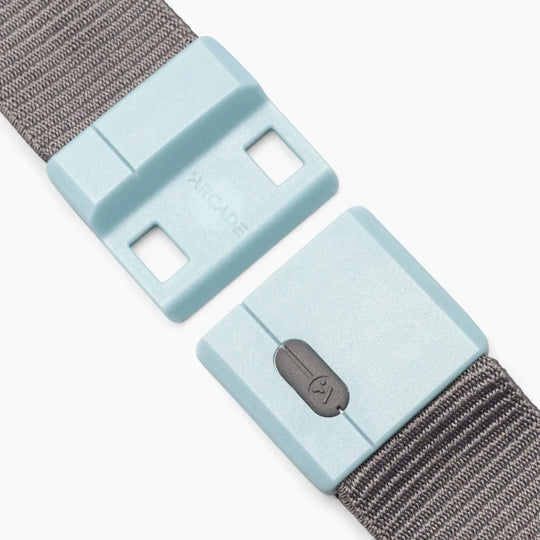 A close-up view of the Arcade Belts Polar Mag, a grey fabric belt featuring a light blue plastic buckle with SwiftLock technology for secure, durable closure. The rectangular buckle is shown detached and displays a small icon resembling a speaker or sound symbol.