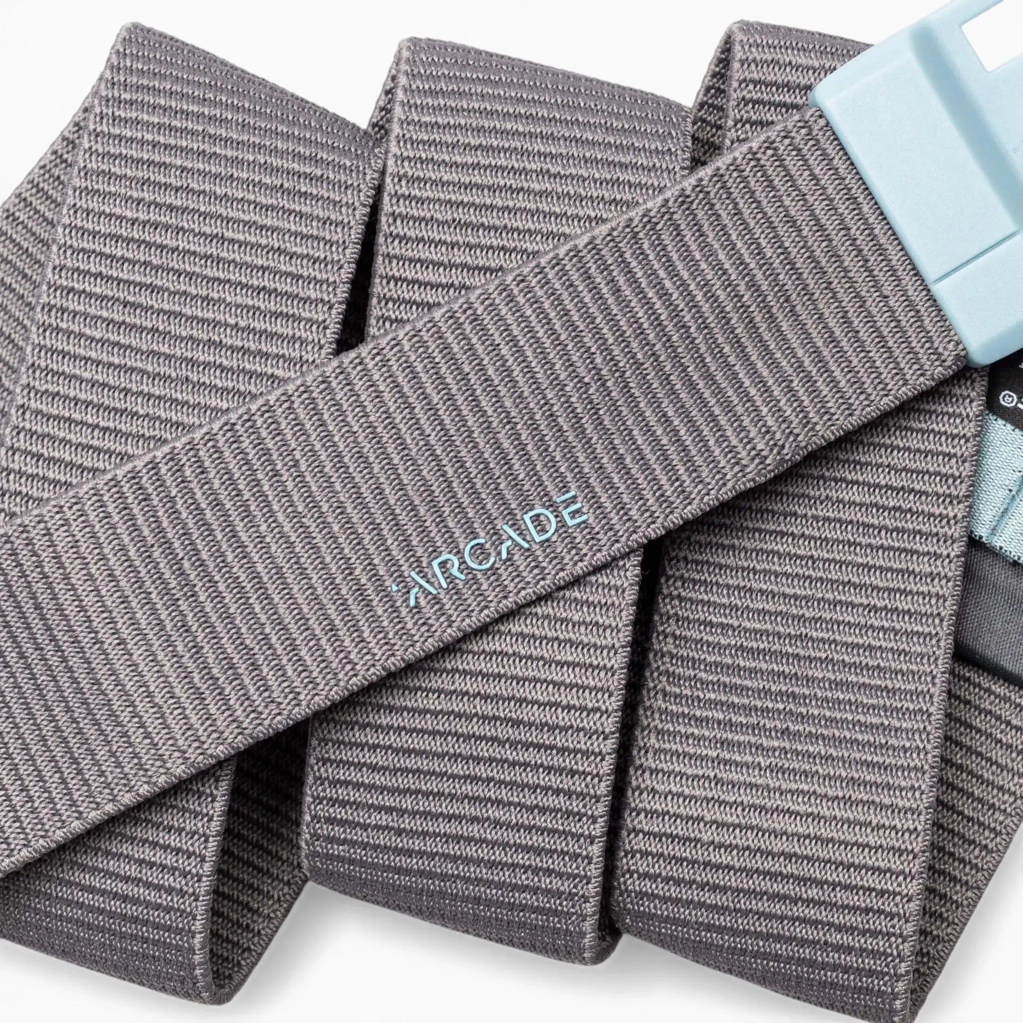 A gray ribbed fabric belt, the Polar Mag by Arcade Belts, is coiled against a white background. The word "ARCADE" is embroidered in light blue on its surface, and the durable light blue buckle features SwiftLock technology for easy, secure fastening.